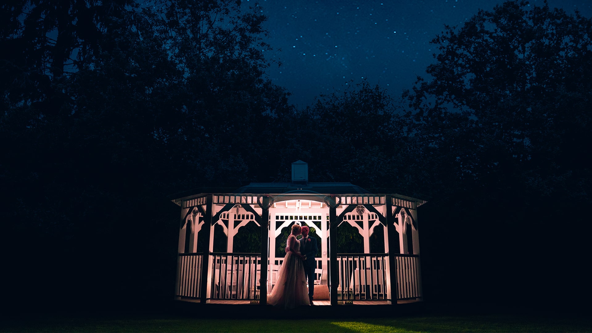bride and groom on a gazebo at night backlit with a light